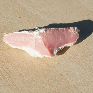 Op de afbeelding: Een ruw gecut stuk roze kwarts in roze en wit op een houten oppervlak.