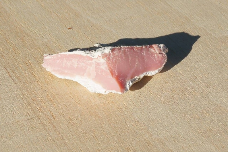 Op de afbeelding: Een ruw gecut stuk roze kwarts in roze en wit op een houten oppervlak.