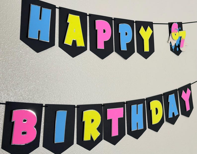 May include: A black banner with the words "HAPPY BIRTHDAY" in colorful, 3D letters. The letters are outlined in silver and have a blue, pink, and yellow color scheme. A small banner with the number "67" is also included.