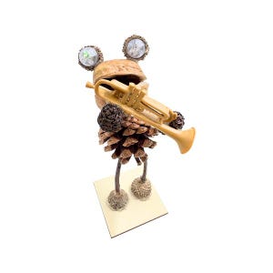 May include: A whimsical figurine of a frog playing a trumpet, made from pine cones, acorns, and other natural materials. The frog is brown and has a gold trumpet.