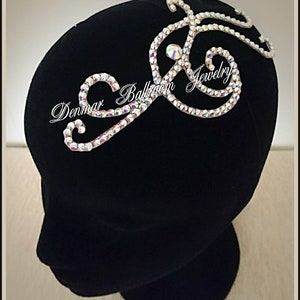 May include: A silver rhinestone hair comb with a swirl design. The comb is on a black velvet mannequin head. The text "Denmar Ballroom Jewelry" is visible on the comb.