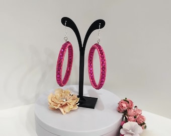 May include: A pair of pink hoop earrings with clear rhinestones. The earrings are on a black display stand.