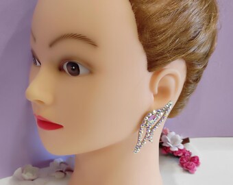 May include: A pair of silver earrings with a crystal design. The earrings are shaped like a wing and have a clear, iridescent finish.