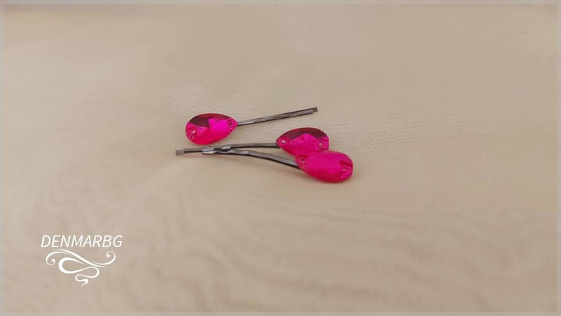 Puede incluir: Tres horquillas rosas fucsia con joyas en forma de l&aacute;grima. Las horquillas son de color plateado y las joyas son de un color fucsia vibrante. Las horquillas est&aacute;n dispuestas sobre una superficie de tono neutro.
