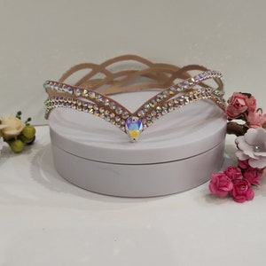 May include: A delicate, brown, rhinestone-encrusted headband with a V-shaped design. The headband is on a white surface.