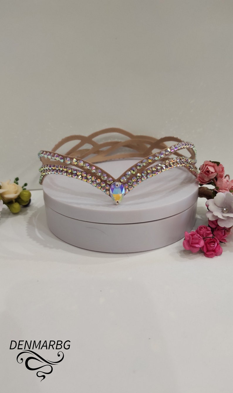 May include: A delicate, brown, rhinestone-encrusted headband with a V-shaped design. The headband is on a white surface.