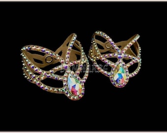May include: A pair of beige dance shoe embellishments with a butterfly design. The embellishments are covered in iridescent rhinestones and have a large, clear rhinestone in the center.
