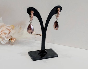 May include: A pair of dangle earrings with a teardrop-shaped crystal in a dark brown color. The earrings are made with a silver-toned metal and have a row of small, clear beads.