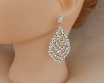 May include: A pair of silver teardrop earrings with a crystal design. The earrings are made of small, clear crystals that are set in a teardrop shape. The earrings are dangling from a silver hook.