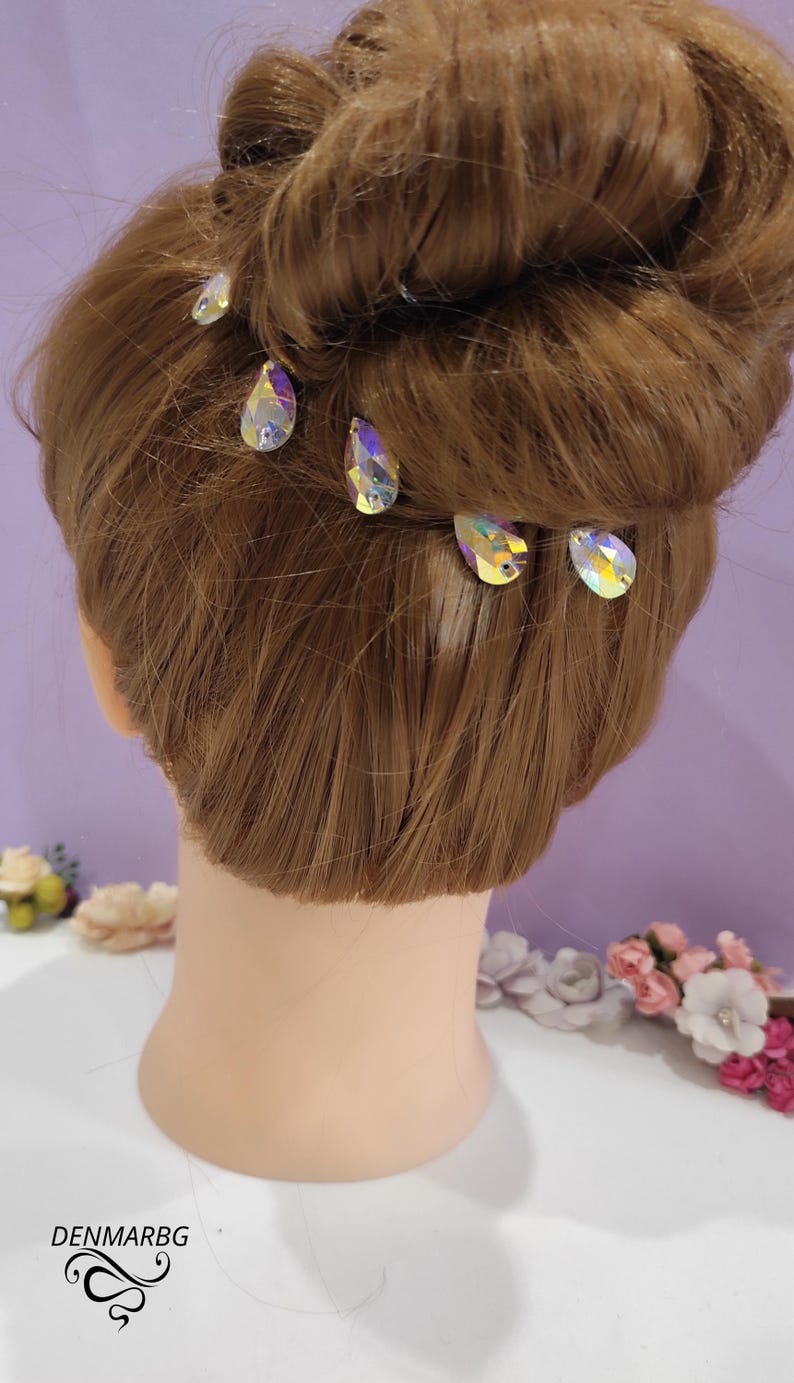 Puede incluir: Una cabeza de maniqu&iacute; con cabello casta&ntilde;o claro peinado en un mo&ntilde;o, adornada con varias horquillas de cristal iridiscente. Los alfileres tienen forma de l&aacute;grima y reflejan m&uacute;ltiples colores. El texto "DENMARBG" es visible.