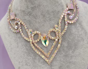 Puede incluir: Un delicado collar de cristal rosa iridiscente con un diseño en forma de V. El collar está hecho de pequeños cristales facetados que están engastados en un metal plateado.