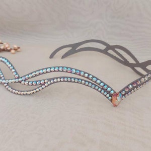 May include: A silver headband with a double row of iridescent rhinestones in a wave pattern. The headband is made of a flexible metal and has a decorative piece at the center.