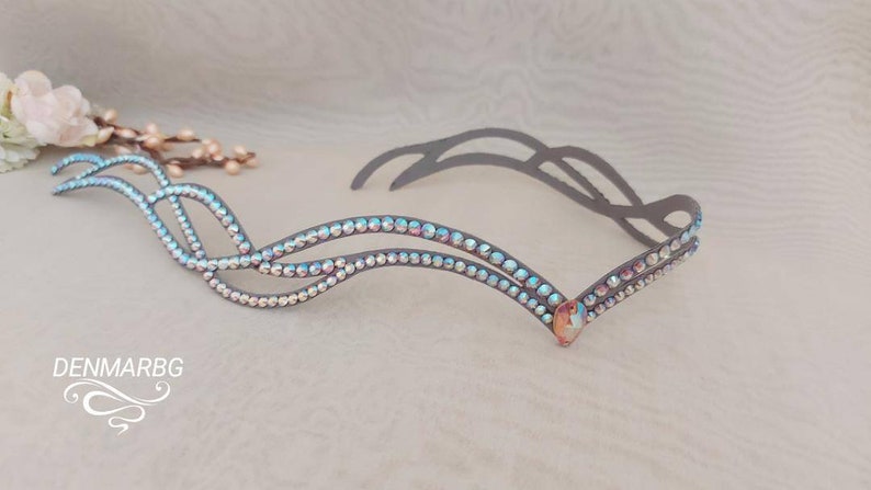 May include: A silver headband with a double row of iridescent rhinestones in a wave pattern. The headband is made of a flexible metal and has a decorative piece at the center.
