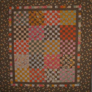 Könnte beinhalten: Eine Steppdecke mit einem karierten Muster in Braun-, Orange-, Rosa- und Gelbtönen. Die Steppdecke ist von einem braunen Rand mit einem Blumenmuster umgeben.