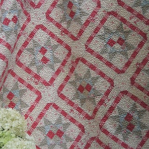 Puede incluir: Una colcha vintage con un patrón de estrellas rojo, blanco y azul. La colcha está hecha de tela de algodón y tiene un aspecto descolorido y desgastado.