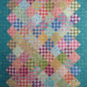 Peut inclure: Une courtepointe colorée avec un motif de patchwork présentant une variété de motifs floraux et de carrés à carreaux. La courtepointe est bordée d'un tissu turquoise.