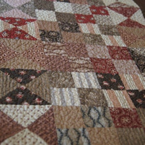 Könnte beinhalten: Eine Decke aus verschiedenen Brauntönen, Rosa- und Rottönen. Die Decke besteht aus Quadraten und Dreiecken, und die Stoffe haben verschiedene Muster, darunter Blumen, Paisley und geometrische Muster.
