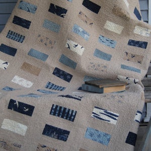 May include: A beige and blue patchwork quilt with a geometric pattern of rectangles. The quilt is made of various fabrics with different textures and patterns, including a fabric with a bird print.