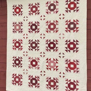 May include: A white quilt with a repeating pattern of red and pink squares. Each square features a smaller red square in the center surrounded by a ring of smaller red triangles.