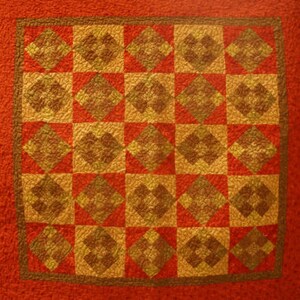 May include: A quilt with a checkerboard pattern of red and gold squares. Each square has a diamond pattern within it.