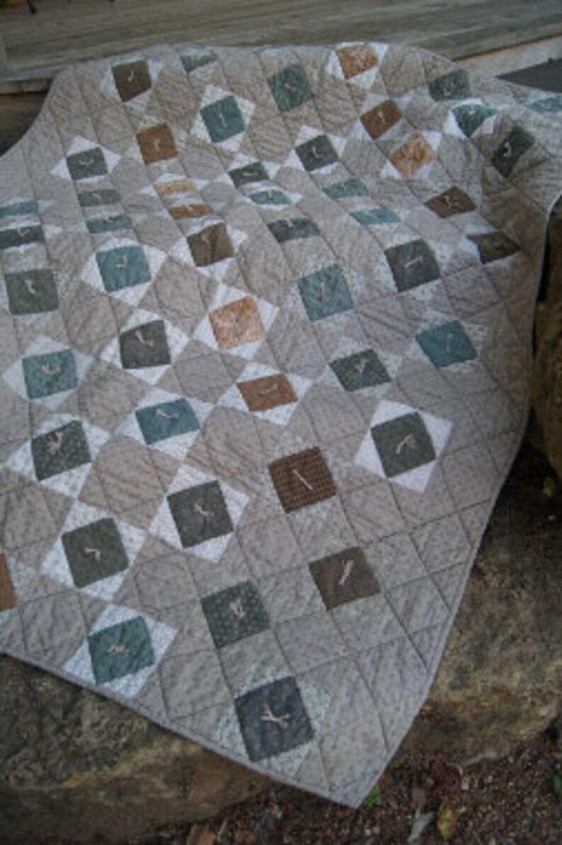 May include: A quilt with a geometric pattern in shades of brown, gray, and blue. The quilt is made of squares and diamonds, and the fabric has a subtle texture.