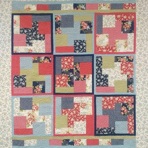 May include: A patchwork quilt featuring a floral design in shades of red, blue and green. The quilt is made up of squares of different fabrics, each with a unique pattern. The quilt is bordered by a white fabric with a small floral pattern.