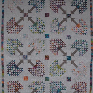 May include: A white quilt with a repeating pattern of colorful trees. Each tree is made up of small triangles in various shades of blue, green, purple, orange, and pink. The trees are arranged in a grid pattern with a gray arrow pointing out from each tree.