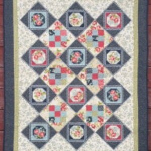 May include: A quilt with a patchwork design featuring floral, plaid, and geometric patterns in shades of blue, red, and white. The quilt is framed with a dark blue border and a light green inner border.