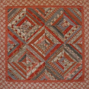 May include: A handmade quilt with a geometric design. The quilt features a central pattern of diamond shapes in shades of red, gray, and cream. The border is a floral pattern in a matching color palette. The quilt is likely made of cotton.