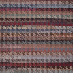 May include: A quilt made of many small fabric squares, each with a different pattern. The quilt is made up of rows of squares, with each row having a different color scheme. The quilt is a mix of brown, red, and blue colors.