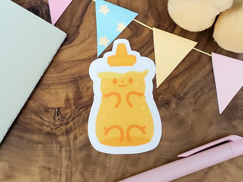 May include: A yellow honey bear sticker with a white outline. The bear is sitting in a honey jar with a white lid. The sticker is on a wooden surface.