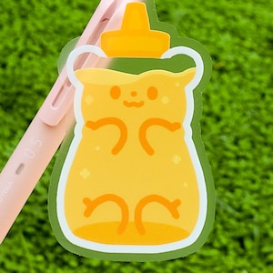 May include: A clear sticker of a cartoon honey bear with a yellow body and a white outline. The bear is smiling and has small, round eyes. The honey bear is wearing a yellow honey pot lid on its head.