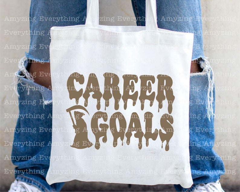 Puede incluir: Una bolsa de tela blanca con un gr&aacute;fico marr&oacute;n que dice "CAREER GOALS" con letras que gotean. El gr&aacute;fico tambi&eacute;n incluye una imagen estilizada de la Muerte.