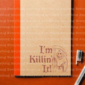 May include: A brown notebook with the text "I'm Killin' It!" printed on the front. The text is in a dark brown font and is surrounded by a black and white illustration of the Grim Reaper holding a scythe.