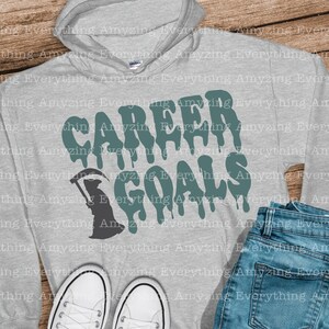 Puede incluir: Una sudadera con capucha gris con el texto "CAREER GOALS" en letras verdes que gotean. Una silueta negra de la Muerte sosteniendo una guada&ntilde;a a la izquierda del texto.