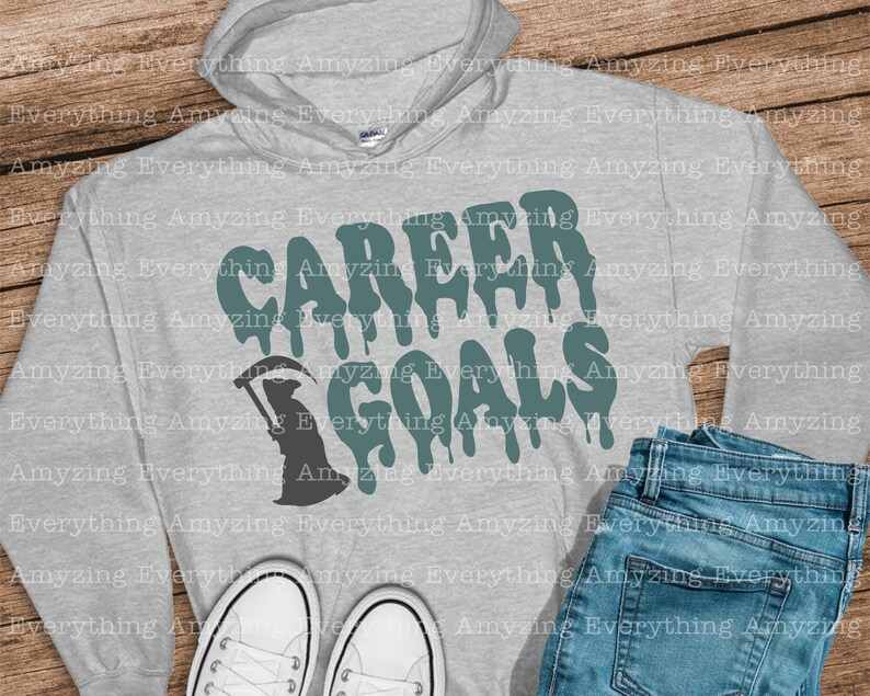 Puede incluir: Una sudadera con capucha gris con el texto "CAREER GOALS" en letras verdes que gotean. Una silueta negra de la Muerte sosteniendo una guada&ntilde;a a la izquierda del texto.
