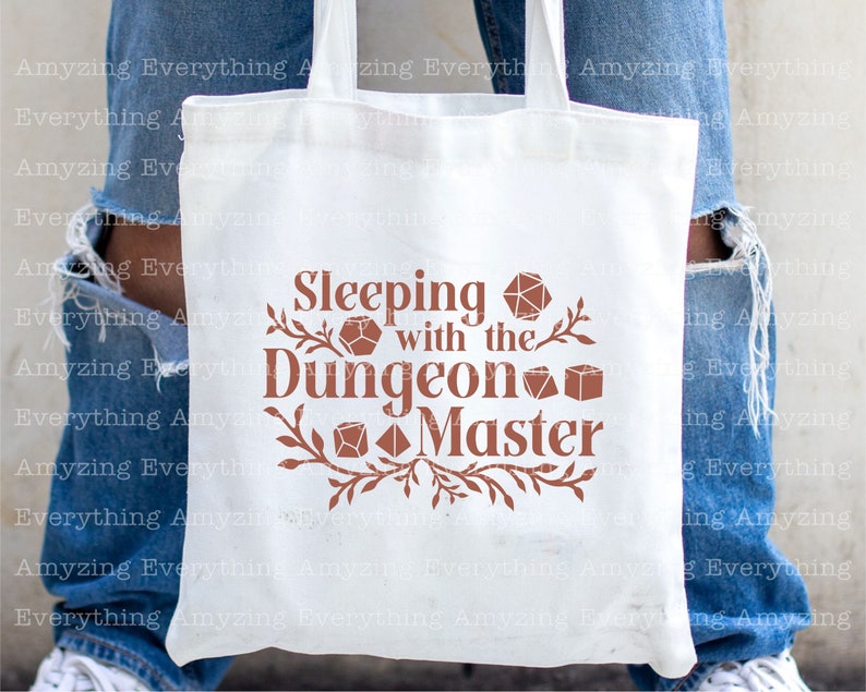 May include: White tote bag with a brown design that says "Sleeping with the Dungeon Master". The design includes stylized dice and vines.