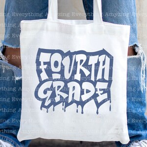 May include: A white tote bag with a blue and white graphic that says "FOURTH GRADE" in a graffiti style font. The bag is being held by a person wearing blue jeans.