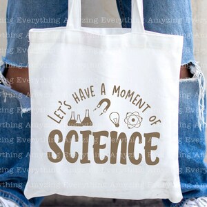 Może przedstawiać: Biała torba typu tote z brązowym tekstem, kt&oacute;ry brzmi "Let's have a moment of science". Tekst jest otoczony obrazami zlewki, żar&oacute;wki, magnesu i atomu.