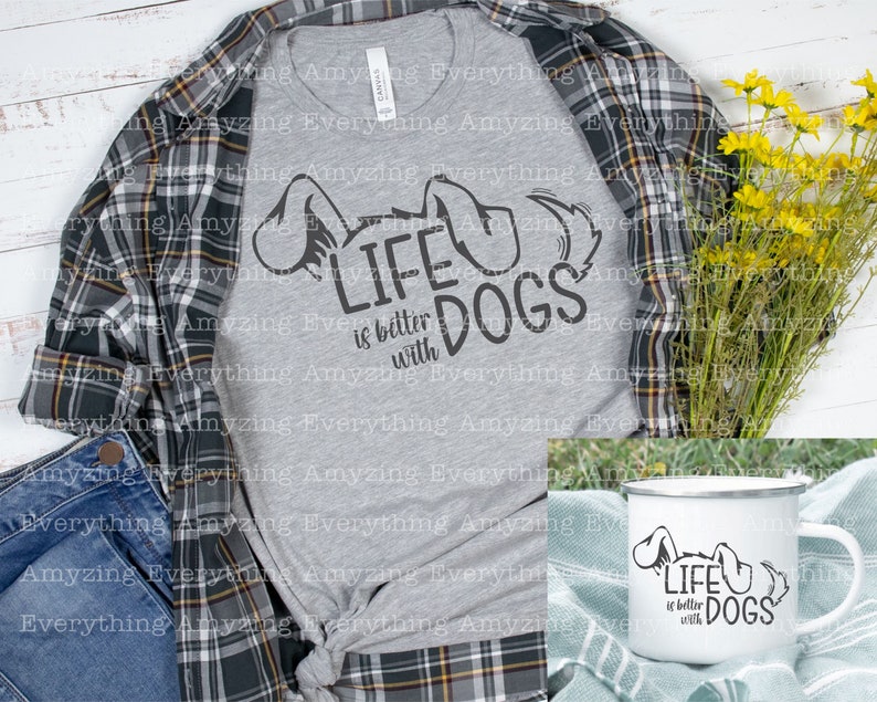 May include: A gray t-shirt with the text "Life is better with dogs" and a dog silhouette. The shirt is displayed on a plaid shirt and a wooden surface. A white enamel mug with the same design is also shown.
