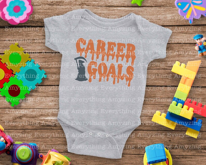 Puede incluir: Un body de beb&eacute; gris con el texto "CAREER GOALS" en letras naranjas que gotean. Una silueta negra de la Muerte est&aacute; a la izquierda del texto.