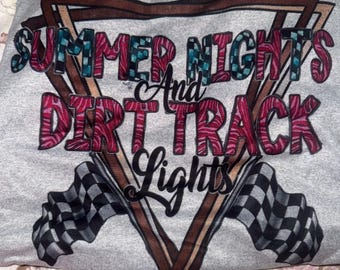 Peut inclure: Un t-shirt gris avec l'inscription "SUMMER NIGHTS DIRT TRACK LIGHTS" dans une police décorative. Le motif comprend des drapeaux à damier et une forme géométrique marron et noire.