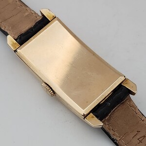 May include: A gold-toned rectangular wristwatch with a black leather band. The watch face is not visible in the image.