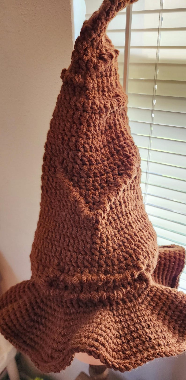 May include: A brown, handmade crochet hat with a pointed top and a wide brim. The hat is made of a textured yarn, and the color is a warm, earthy brown. The hat is likely a costume or novelty item.