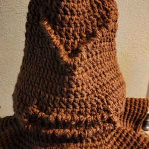 May include: A handmade, brown crocheted hat with a pointed top and a textured, woven appearance. The hat has a wide brim and is made of a soft, warm material, perfect for cold weather. The hat is a unique, handcrafted item.