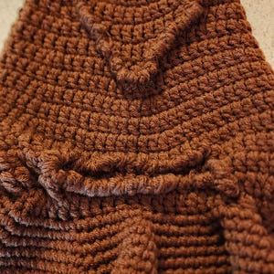 May include: Close-up of a brown crocheted hat with a textured surface. The hat features a detailed, raised design, possibly a tree or leaf pattern, adding a unique touch to the handmade item.