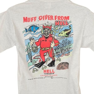 May include: A light gray t-shirt with a graphic on the back featuring a devil diver with a trident and the text "Muff Diver From Hell" and "Hell Township Cayman Islands". The graphic includes cartoon fish and coral.