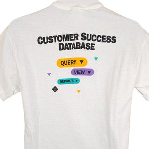 May include: White t-shirt with the text "CUSTOMER SUCCESS DATABASE" printed on the back. The text is in black and is surrounded by colorful icons that say "QUERY", "VIEW", and "REPORTS".