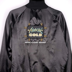 Op de afbeelding: Zwarte satijnen bomberjack met een geborduurd Apache Gold Hotel Casino Resort logo op de rug.