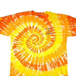 Peut inclure: T-shirt tie-dye jaune et orange avec un petit logo sur le devant qui dit "On Caromace, Key West, Florida, 1-800-633-3047".